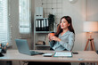 © Crystal - Young Asian business woman relaxing at office desk, holding coffee cup and looking away, taking a pleasant break from work