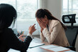 © Crystal - Young businesswoman experiencing stress and burnout, covering her face in frustration during a difficult conversation with a colleague
