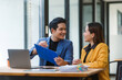© Crystal - Two Asian businesspeople reviewing documents and discussing work, showing successful teamwork and professional collaboration in a modern office setup