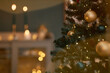 © Seventyfour - Christmas tree decorated with gold and dark ornaments standing indoors with string lights glowing, blurred background showing warm lights and festive atmosphere, no people visible