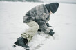 © Seventyfour - Caucasian boy crouching on snowy ground shaping snow with hands outdoors during winter, wearing warm clothing and knit hat, focusing on activity