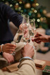 © Seventyfour - Multiethnic group of young adult men and women clinking champagne glasses together in celebration, hands visible in foreground with festive decorations in background