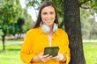 © Raquel - Happy caucasian woman wearing yellow shirt holding digital tablet and smiling outdoors in sunny green park,technology and lifestyle concept, natural background for design or promotional template.