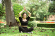 © WMSTUDIO - Young woman practicing yoga in serene outdoor setting surrounded by trees and green grass, embodying peace and mindfulness through meditation
