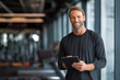© tynza - Portrait of confident fitness coach holding tablet in modern gym, clean design, professional look