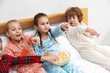 © New Africa - Cute children in pajamas eating popcorn while watching movie on bed at home