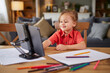 © Stockphotodirectors - A young child engages in drawing at a kitchen table, focused on a tablet while colorful markers and sheets of paper surround them, creating a lively family atmosphere.