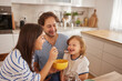 © Stockphotodirectors - A woman happily feeds her smiling child in a bright kitchen while a man watches with delight. The family enjoys a warm, loving moment during breakfast.