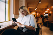 © BullRun - Relaxed woman sitting in cafe near window and using smartphone for work communication, representing digital lifestyle, remote connection, and mobile productivity