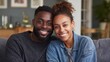 © Johannes - portrait of multiethnic couple embracing and looking at camera sitting on sofa smiling african american woman hugging mid adult man sitting on couch from behind at home happy mixed race couple laugh