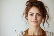 © stockphoto02 - A captivating portrait of a young artist with reddish-brown hair, light eyes, and soft freckles, holding paintbrushes and smiling warmly.