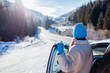 © maryviolet - Back view of woman traveler admiring snowy mountains walking out of car looking at winter landscape. Traveling by auto
