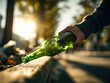 © Daria - Person discarding a green glass bottle on the street during sunset