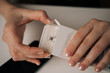 © dikushin - Close-up female hands with manicured nails carefully opening white retail package containing new phone adapter cable, ready to connect and charge. Concept of smartphone unboxing process.