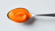 © Nurul - Close-up shot on white showing a spoon holding vibrant orange, smooth puree. The spoon is centered, angled slightly across. High-angle, overhead view