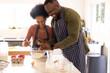 © Wavebreak Media - Diverse couple wearing striped aprons cracking eggs and whisking at kitchen island with mixing bowl