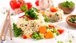 © Bima - A white plate holds a dome of rice with mixed vegetables, beside another, and garnished with herbs. Fresh ingredients include tomatoes, peas, and broccoli