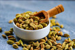 © Creative Canvass - Heap of green cardamom seeds in bowl with wooden spoon on blue background