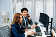 © InfiniteFlow - Smiling Asian businessman calling to broker dynamic stock exchange database with woman business partner pointing to screens comparing profit value online application program at home office. Infobahn.