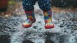 © Stanislau - Child joyfully splashing in a puddle while wearing colorful rain boots during a rainy day in a garden setting