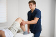© Василь Івасюк - Physiotherapist examining patient knee joint during rehabilitation therapy session in modern medical clinic. Man receiving orthopedic treatment and physical therapy for injury recovery.