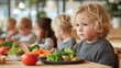 © Oulaphone - A thoughtful child sits at a table with healthy food, surrounded by other children, reflecting a moment of contemplation during mealtime.