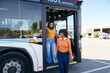 © Koldo_Studio - Two young women friends getting off a modern electric city bus, traveling and using public transportation for urban commuting