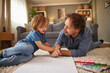 © Stockphotodirectors - A father and child engage in a playful drawing session on the floor of their living room, surrounded by colored pencils and a large sheet of paper. They share smiles and creativity.
