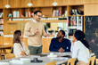 © bnenin - A Man Leads a Group Discussion During an Office Meeting In Bright Library Café With Colleagues Present