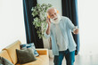 © deagreez - Happy senior man with white beard listens to music on bright orange headphones while holding a smartphone at home smiling