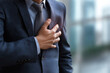 © tynza - Man in business suit sweating and clutching his chest during a panic attack at work, blurred office background