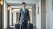 © Tatiana - Asian man bellboy carrying two suitcases in a hotel corridor for guest service. Hospitality professional concept for tourism and travel industry.