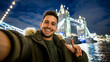 © Davide Angelini - Happy man taking selfie in front of Tower Bridge in London, England - Holidays, travel and technology concept