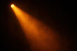 © Chanita - Orange stage spotlight beam cutting through dark atmosphere. Dramatic lighting for concert or theater creates mysterious and focused mood, highlighting an empty space