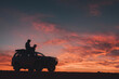© AnnaStills - Silhouette of young adult man sitting on top of SUV using laptop during vibrant sunset, dramatic sky in background, outdoor remote work or travel adventure concept