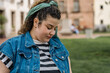 © Jorge - Young woman wearing denim vest looking down contemplating in urban park