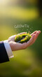 © Mirivox - Hand holding moss with flowers, showcasing new life. The word 'Growth' made of water drops symbolizes development, progress, and potential for future success
