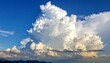 © nora - Fluffy white cumulonimbus cloud dominating a bright blue sky over a blurred mountain silhouette horizon