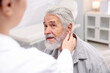 © New Africa - Doctor putting hearing aid into senior man's ear in hospital, closeup