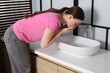 © New Africa - Woman suffering from nausea over sink in bathroom