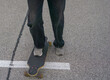 © Lana Pietukhova - low angle close up of a persons feet in gray sneakers standing on a dark longboard on asphalt, white parking space line running under the board, concept of action sports