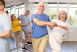 Group of elderly men and woman in sportswear learning to dance latin salsa dance in dance class