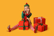 © Pixel-Shot - Young woman in elf costume with Christmas gift boxes on yellow background