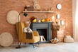 © Pixel-Shot - Interior of living room with armchair, lamp, pumpkins and autumn home decor on fireplace near brick wall