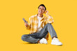 © Pixel-Shot - Young Asian man with TV remote controller and headphones sitting on yellow background