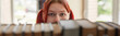 © Seventyfour - Portrait of Caucasian teenage girl with red hair looking directly at camera through row of books on shelf, eyes visible above books, standing in library or bookstore setting