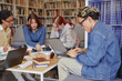 © Seventyfour - Group of multiethnic teenagers collaborating on project, working with laptops and notebooks in library setting, focused on studying and sharing ideas around table