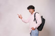 © GAJENDRRA BHATI  - Happy indian college student with backpack pointing at blank space for advertisement isolated on white background. Smiling young asian adult boy looking at camera, look here pose, Education concept