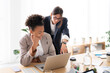 © Studio Marmellata - Two diverse businesswomen collaborate on a laptop in a bright office. One sits smiling while the other points at the screen, discussing their project.
