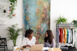 © Studio Marmellata - Two diverse young women collaborate at a modern office desk. One gestures while discussing ideas with her colleague, who listens intently. They work with a laptop and notebooks in a creative space.